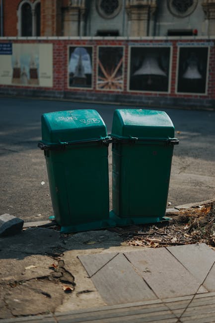 Photograph of the rear side of a white commercial van parked on a street, with three large blue rubbish bags placed on the ground beside the vehicle. The bags are made of plastic, slightly crinkled, a